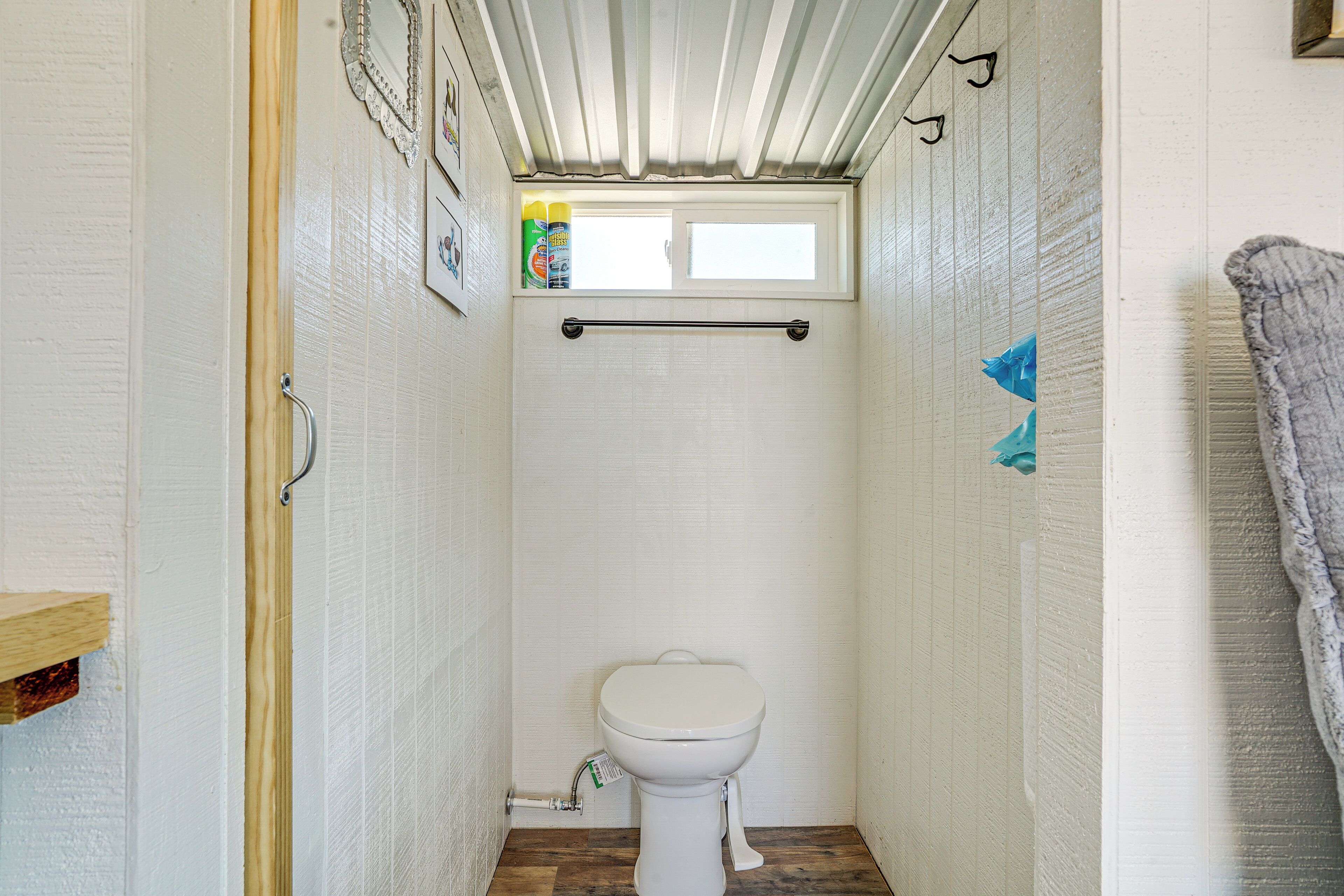 A small, narrow bathroom with a toilet, a window, and a towel rack.