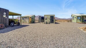 Ein Kiesparkplatz mit mehreren kleinen Gebäuden, darunter ein grünes Bauwerk mit Tür und Fenstern, sowie ein gelber Traktor.