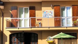 Un edificio a due piani con un balcone, un ombrellone verde e un cartello pubblicitario per la colazione.