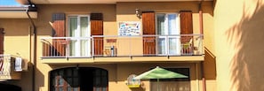 A two-story building with a balcony, a signboard, and a green umbrella.