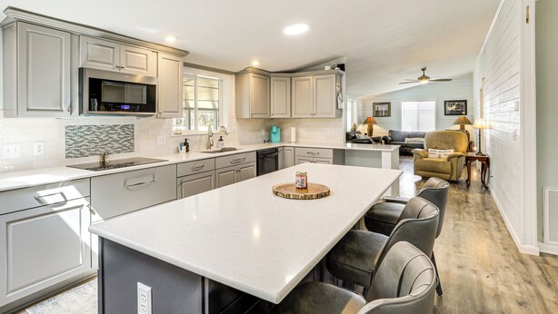 A modern kitchen with grey cabinets, a large island, and a dining area with a yellow armchair. - Lake Moultrie Access: Moncks Corner Home w/ Dock (Moncks Corner)