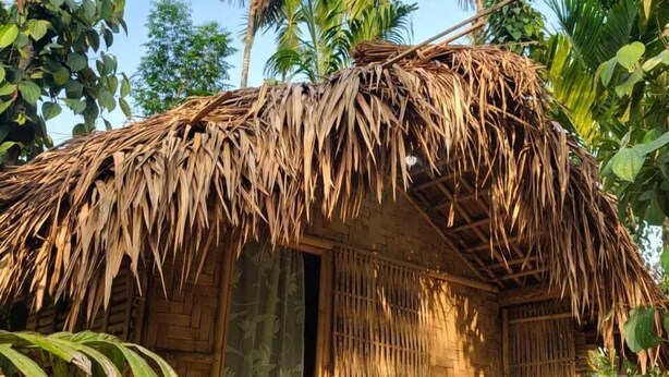 A thatched-roof hut with a wooden floor, surrounded by tropical vegetation. - Warichora Homestay and Rooms Meghalaya (South Garo Hills)