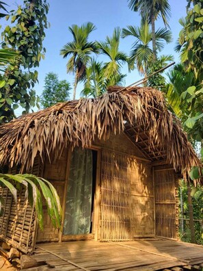 Una capanna con tetto di paglia e pavimento di legno, immersa nella vegetazione tropicale.