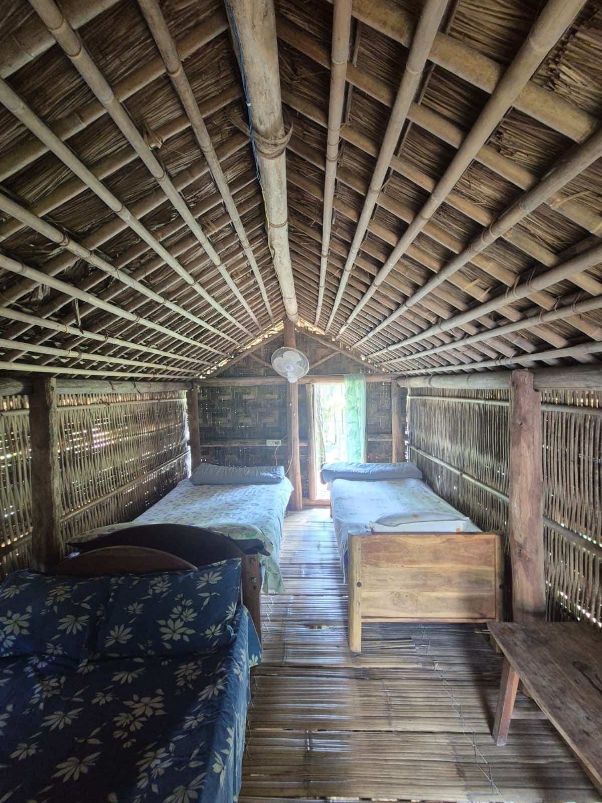 A room with two beds, a wooden bench, and a fan on the ceiling.
