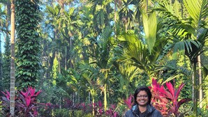 A person standing on a dirt path surrounded by lush greenery and palm trees. - Warichora Homestay and Rooms Meghalaya (South Garo Hills)