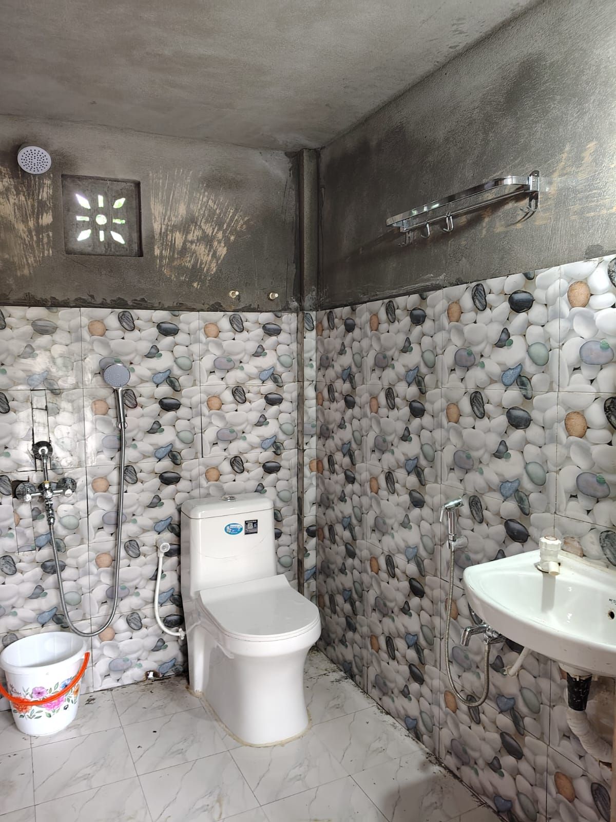 A bathroom with a toilet, shower, and sink, all with a pebble tile backsplash.