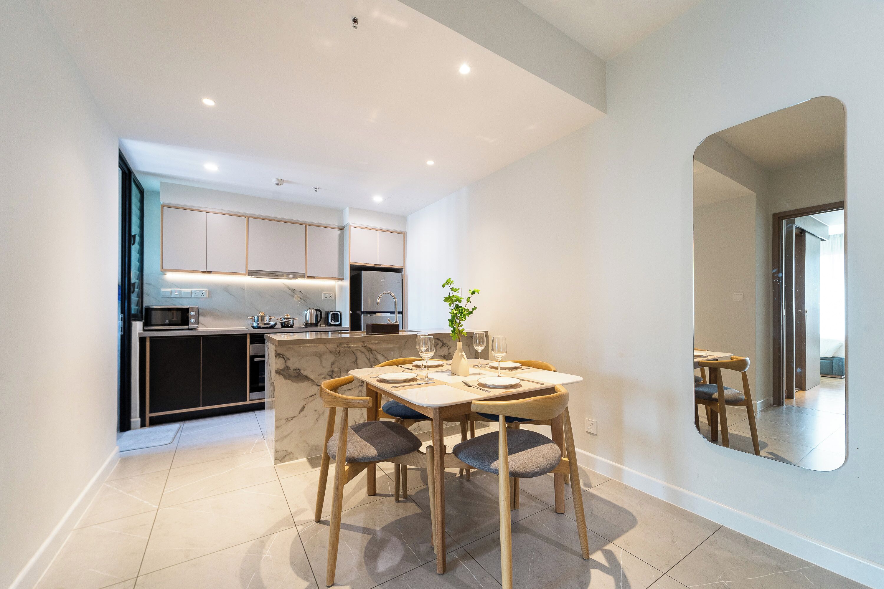A modern kitchen with white cabinets, a marble countertop, and a dining area with a table set for four.