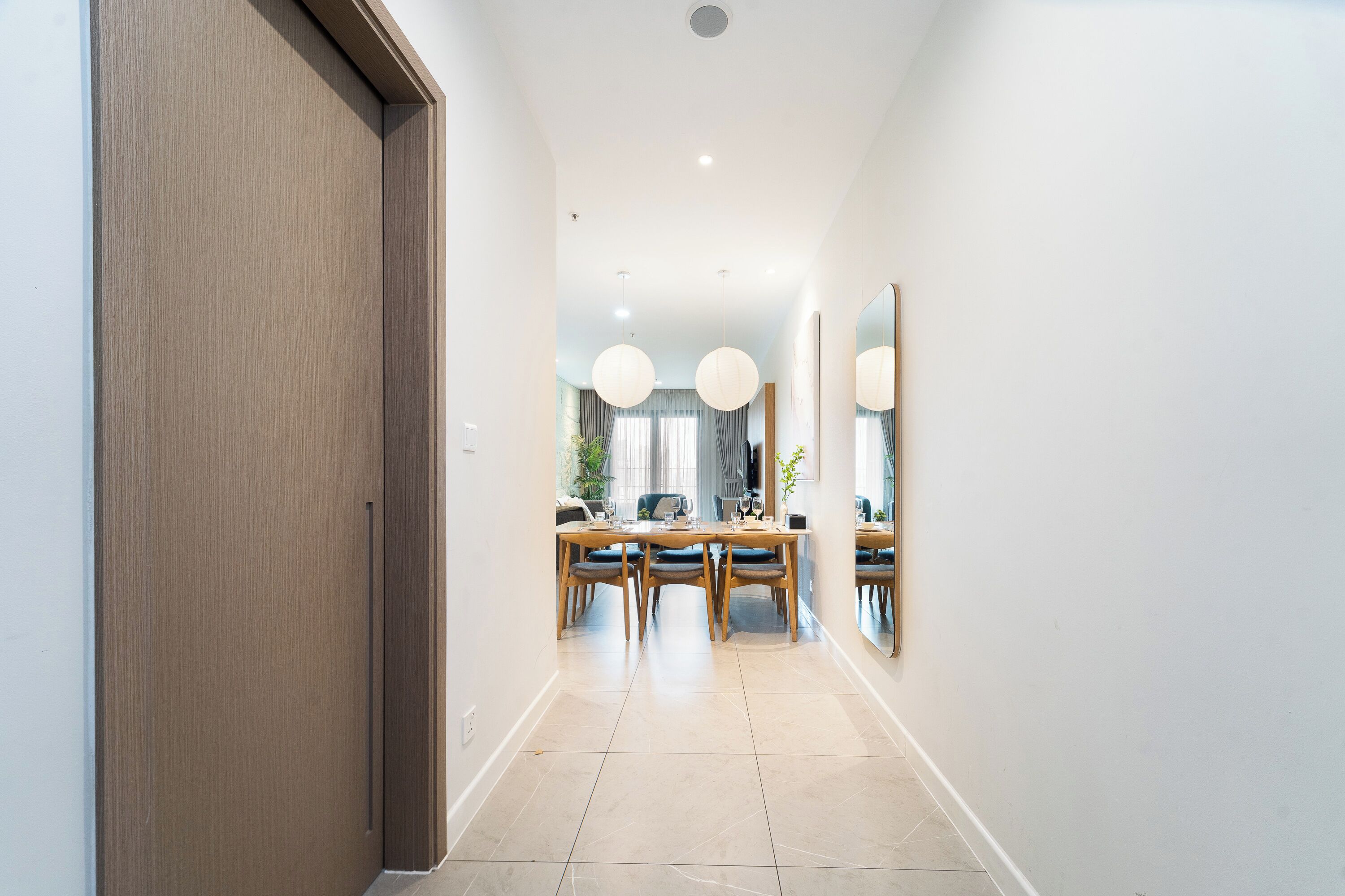Un couloir moderne avec une porte en bois, un coin repas avec une table et des chaises, et un grand miroir accroché au mur.