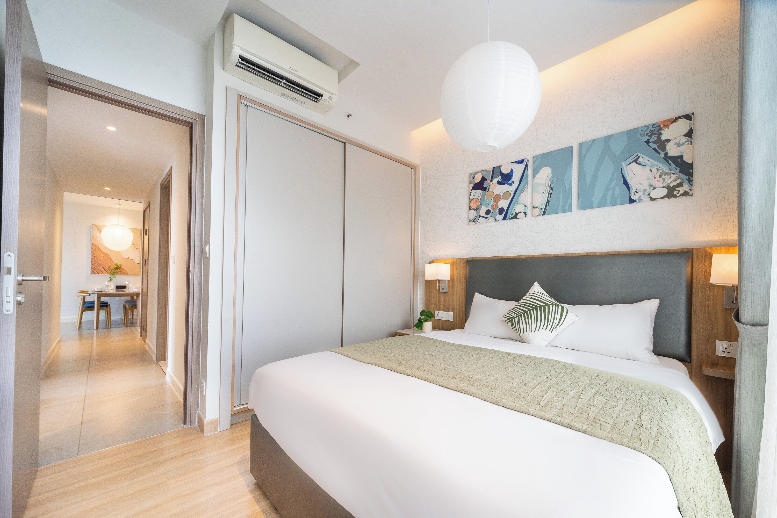 A modern hotel room with a large bed, a desk, and a dining area in the background.