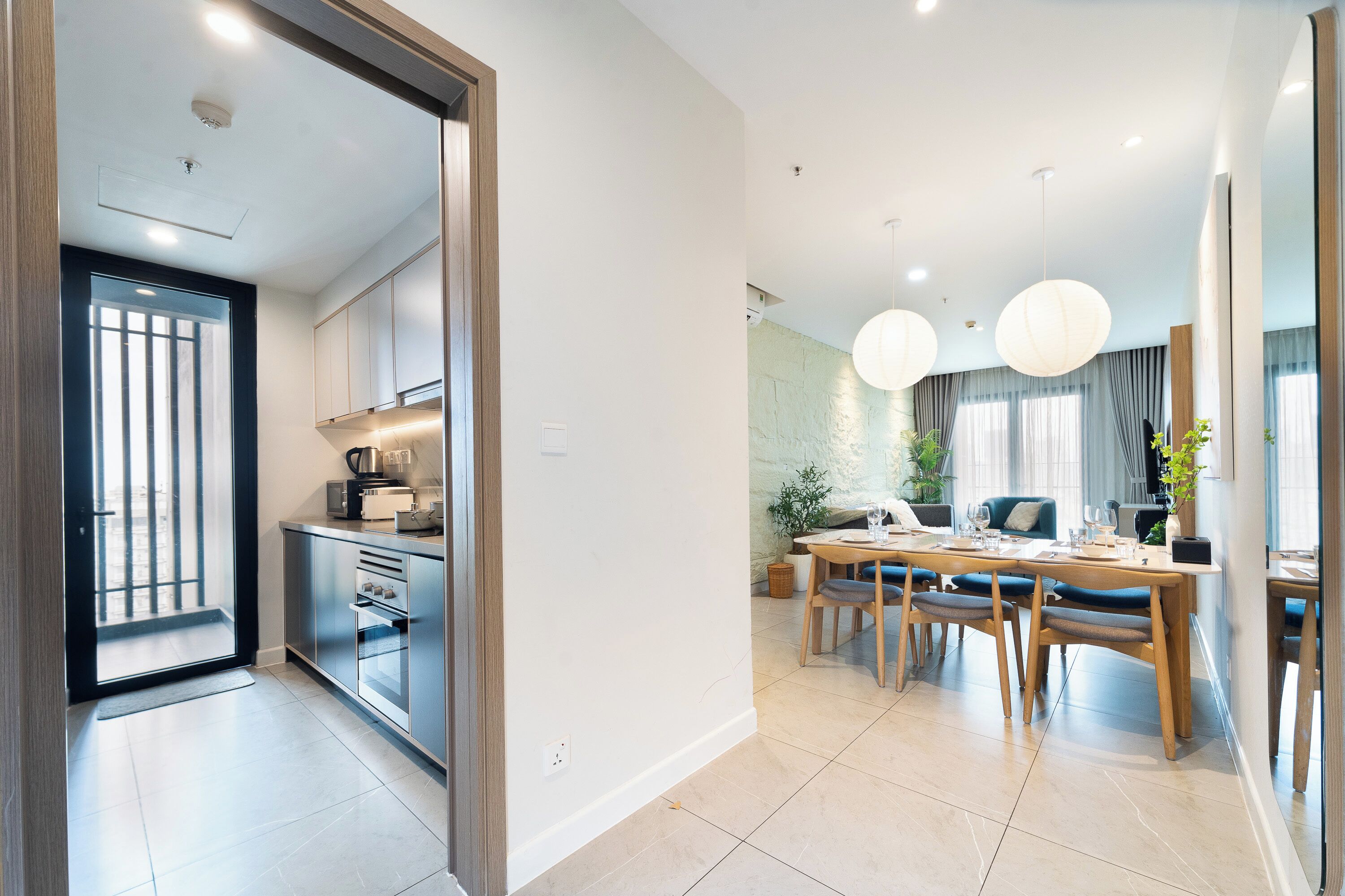 A modern kitchen with stainless steel appliances, a dining area with a wooden table and chairs, and a large mirror reflecting the room.