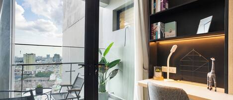 Una habitación moderna con balcón, un escritorio con lámpara, una estantería y una planta en maceta.