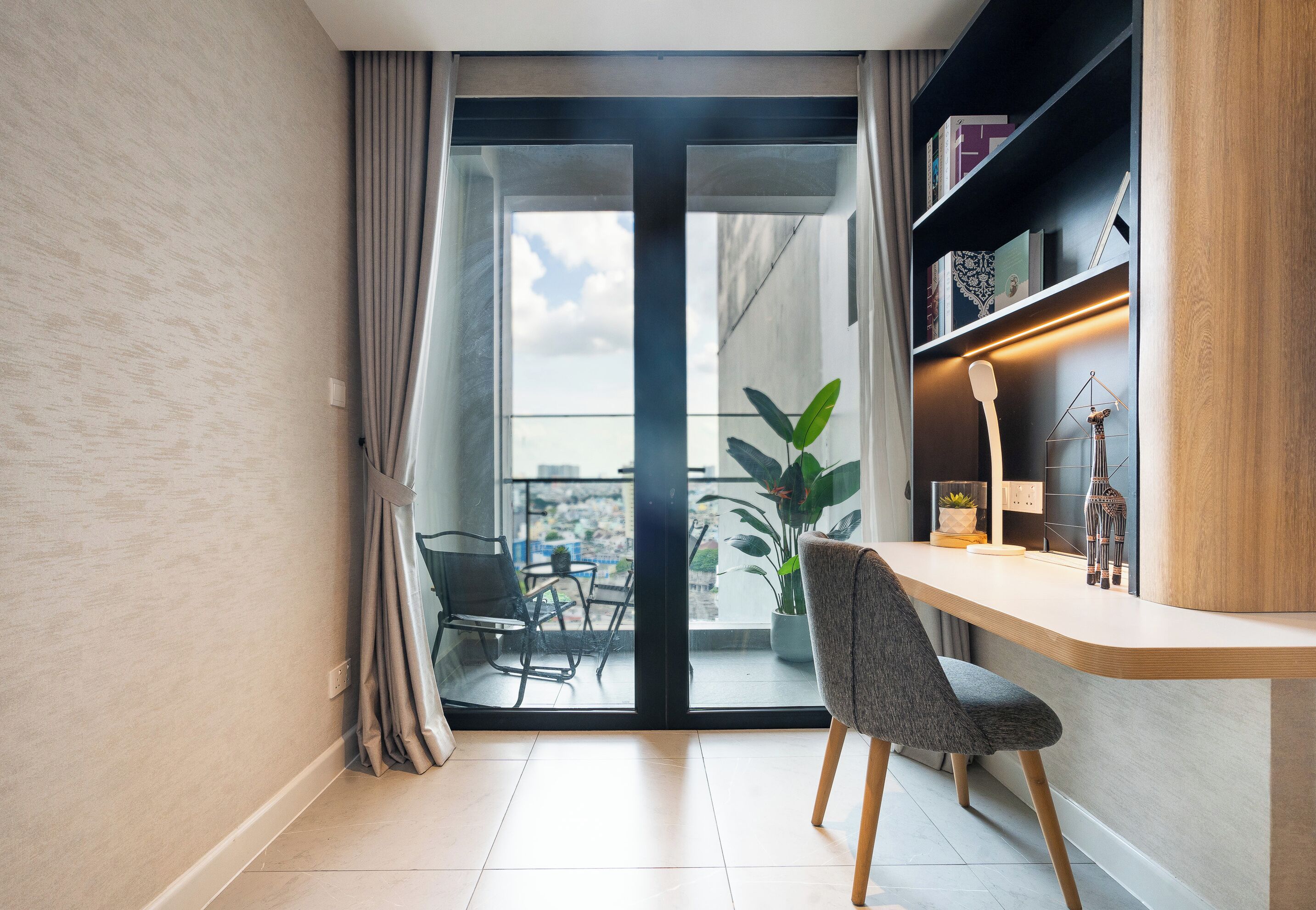 A modern room with a sliding glass door leading to a balcony, a wooden desk, a chair, and a bookshelf.