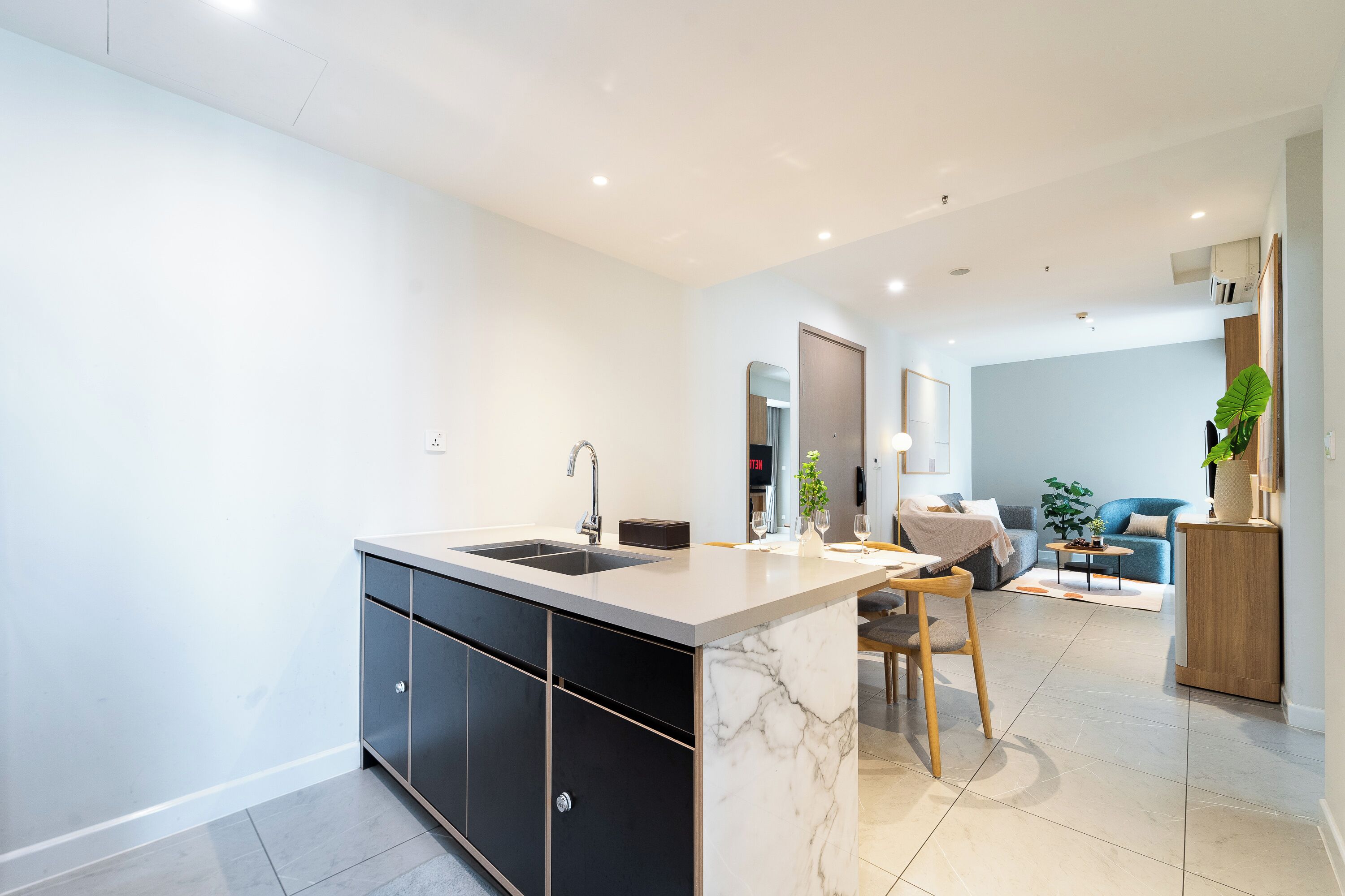 Una cocina moderna con una isla de mármol, gabinetes negros y un comedor con mesa y sillas.