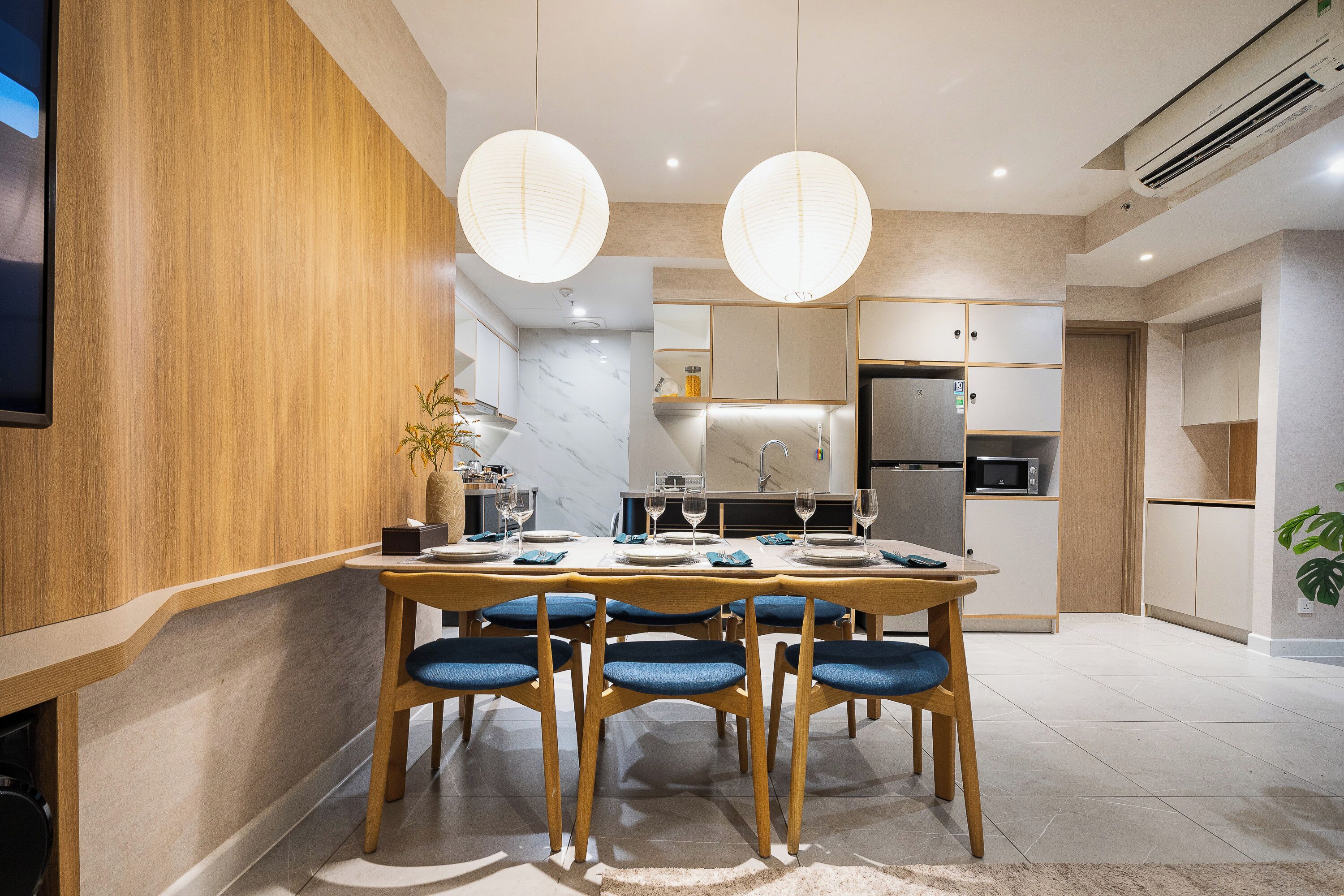 A modern kitchen with a dining area, featuring a wooden table, blue chairs, and pendant lights.