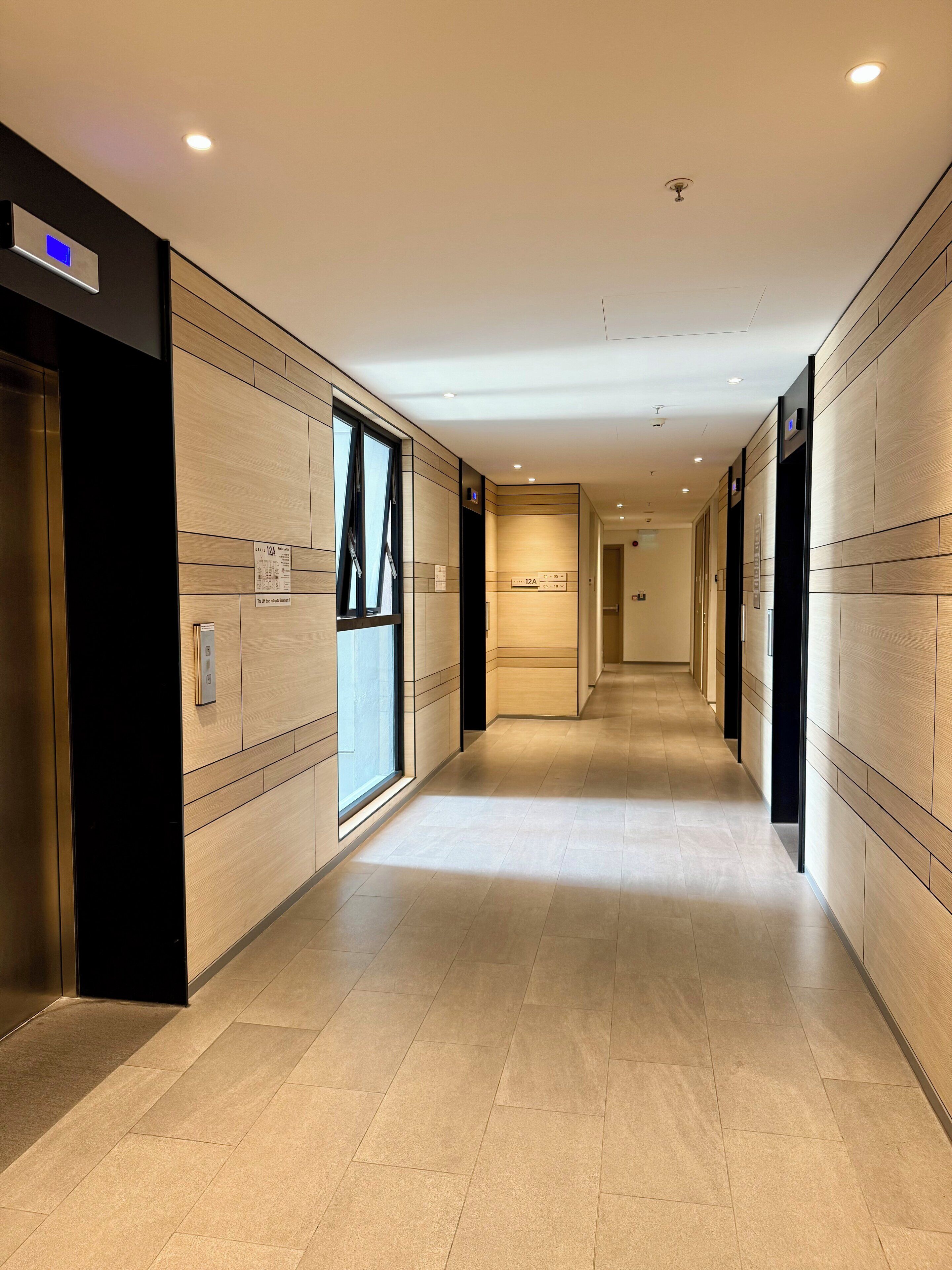 A modern hotel corridor with wooden panel walls, floor-to-ceiling windows, and a long, straight layout.