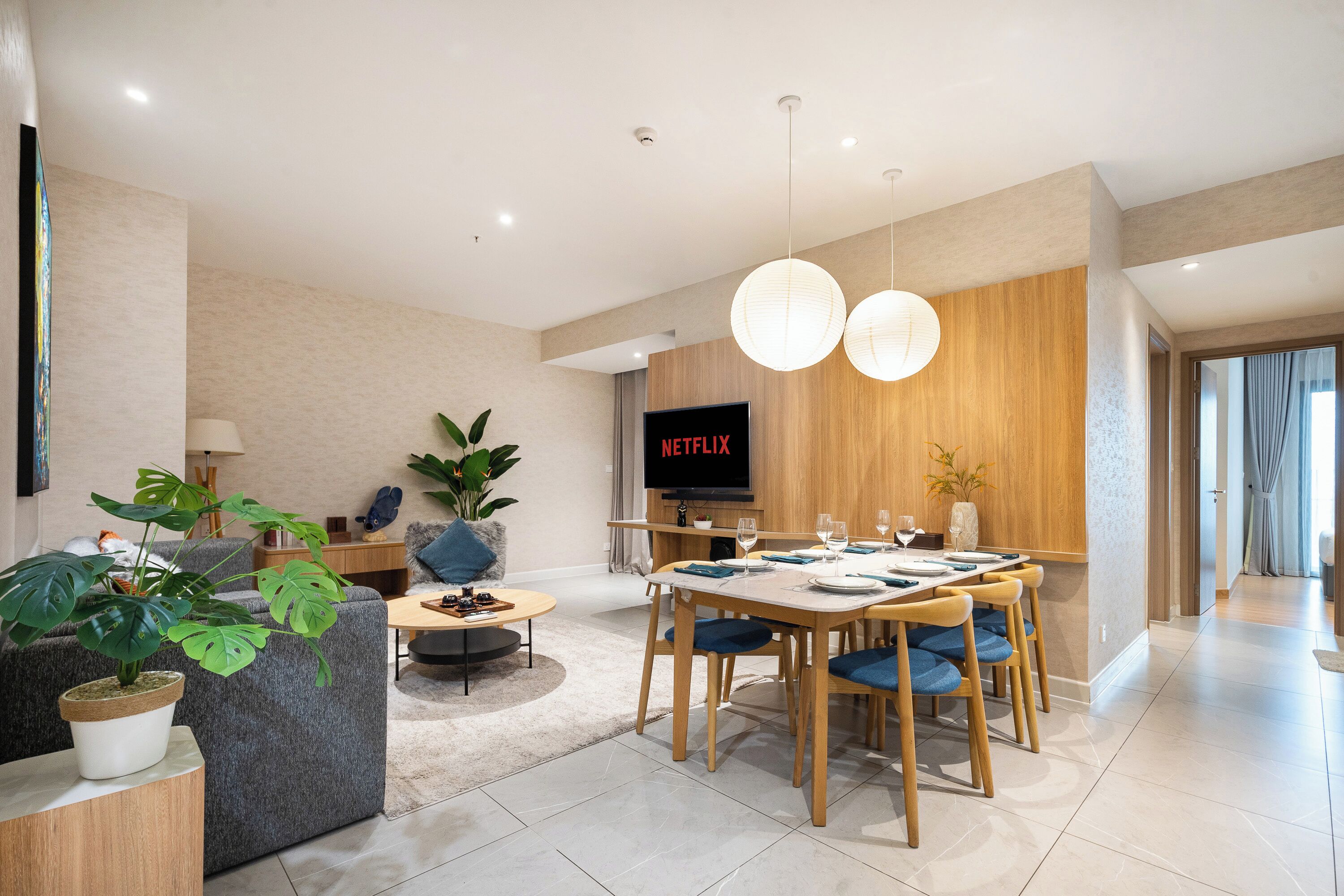 A modern living room with a dining area, a flat-screen TV, and a potted plant.