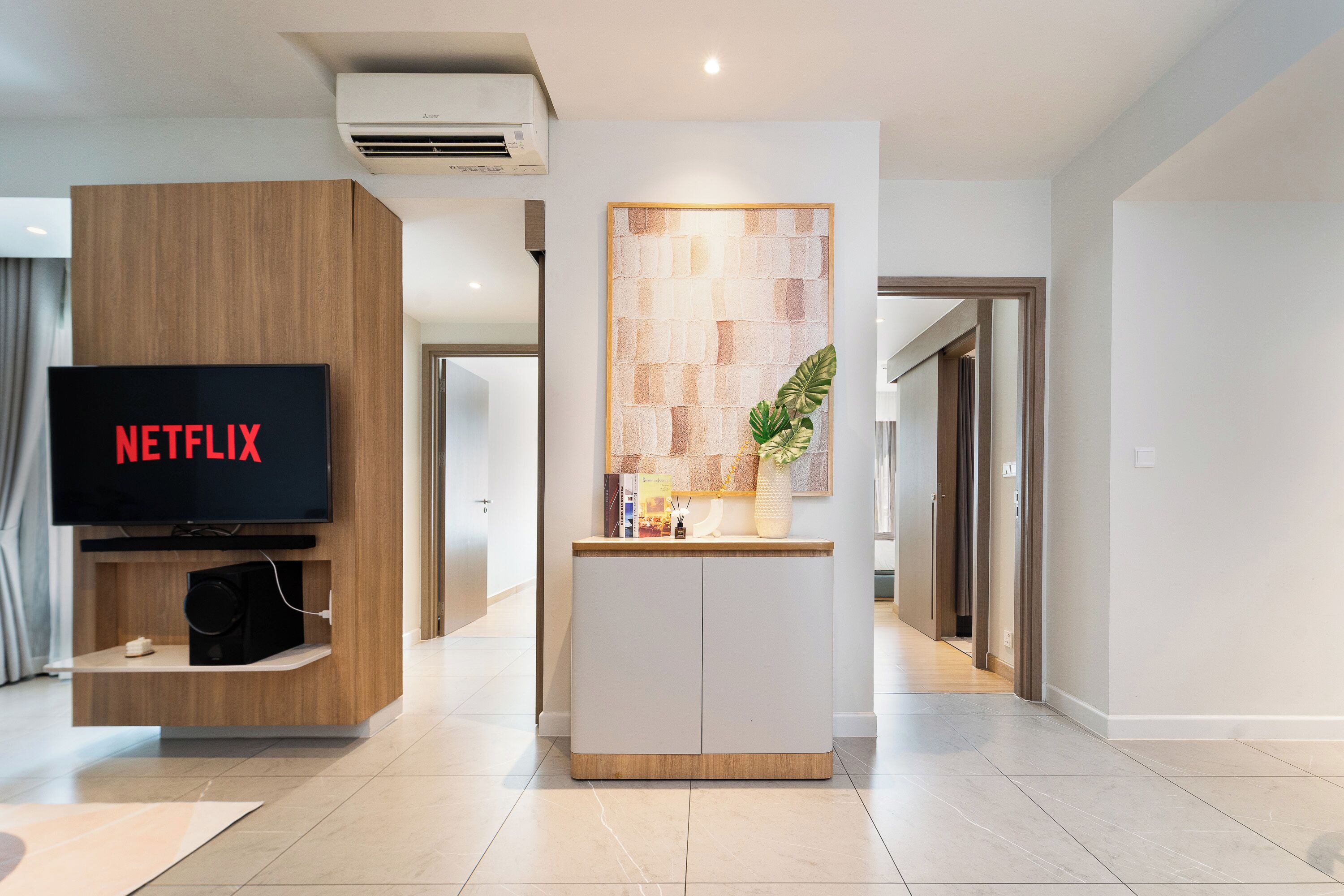 Un salón moderno con una televisión empotrada mostrando 'NETFLIX', un mueble de madera y una consola blanca con objetos decorativos.