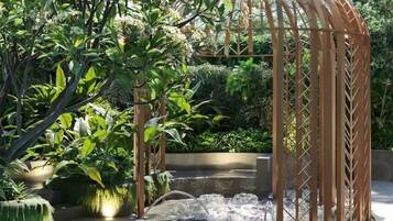 A pool area with a wooden pergola, lush greenery, and a water feature.