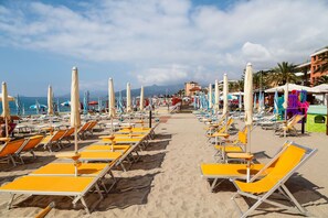 A beach with rows of sun loungers and umbrellas, a clear sky, and a distant mountain. - La Pietra sul Mare in Pietra Ligure (Pietra Ligure)