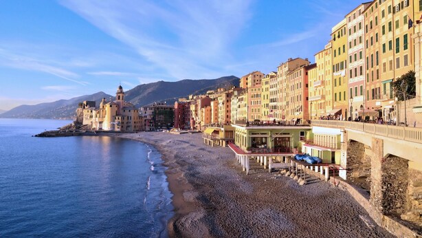 Une ville côtière aux bâtiments aux couleurs vives, qui bordent la plage, avec un clocher imposant et un pont reliant les différentes constructions.