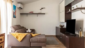 A modern living room with a sectional sofa, a flat-screen TV, a wooden cabinet, and a mounted shelf with decorative items.