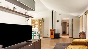 A modern living room with a flat-screen TV, a sofa, a dining area, and a kitchen area.