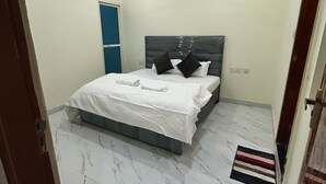 A bedroom with a bed, a ceiling fan, a blue door, and a marble floor. - Narayan Stay (Varanasi)