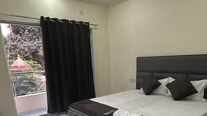 A bedroom with a bed, a ceiling fan, and a balcony with curtains. - Narayan Stay (Varanasi)
