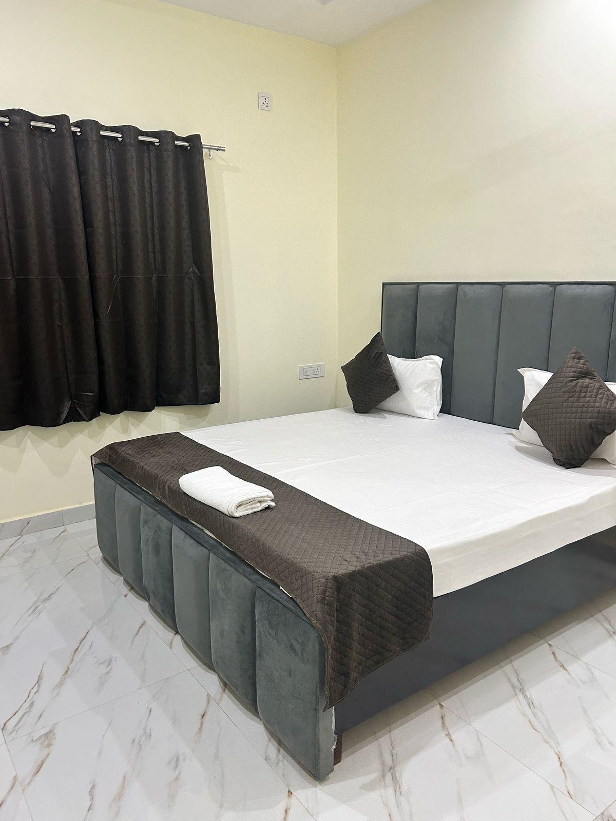 A bedroom with a large bed, a bedside table, a headboard, and a window with curtains.