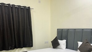 A bedroom with a large bed, a bedside table, a headboard, and a window with curtains. - Narayan Stay (Varanasi)