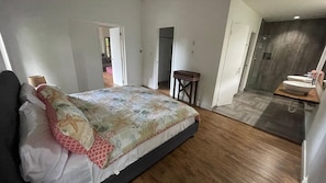 A bedroom with a bed, a wooden floor, a bathroom with a sink, and a door leading to another room. - Gemini Villas Gemini I (Saboga)