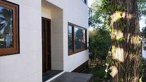 A modern building with large windows, a door, and a tree with vines. - Gemini Villas Gemini I (Saboga)
