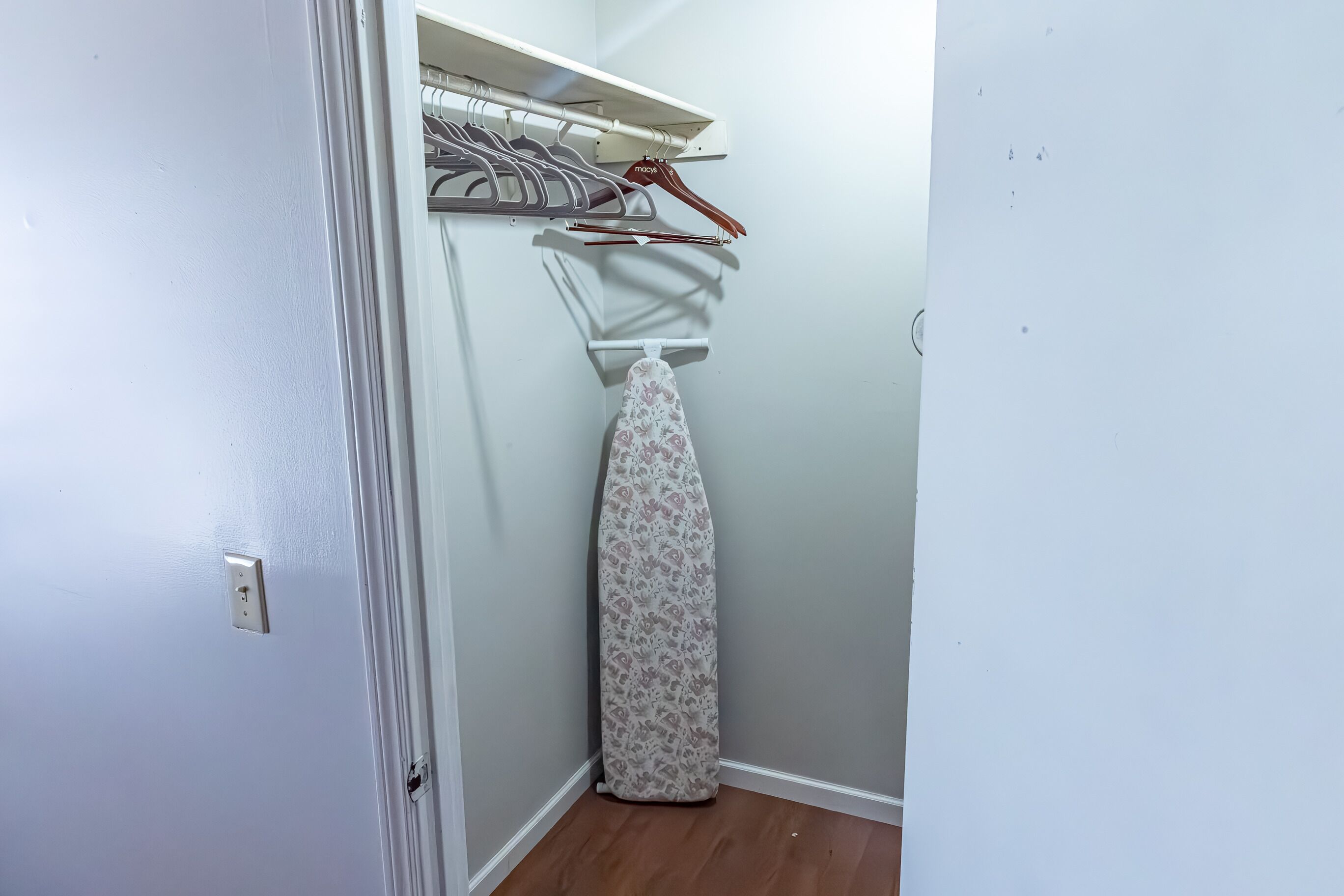 A corner of a room with a hanging clothes rack, a patterned ironing board, and a white door.