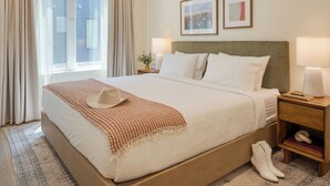 A hotel room with a large bed, two bedside tables, a nightstand, a window with curtains, and two framed pictures on the wall.