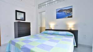 A bedroom with a bed, a dresser, a mirror, and a picture of a coastal scene.