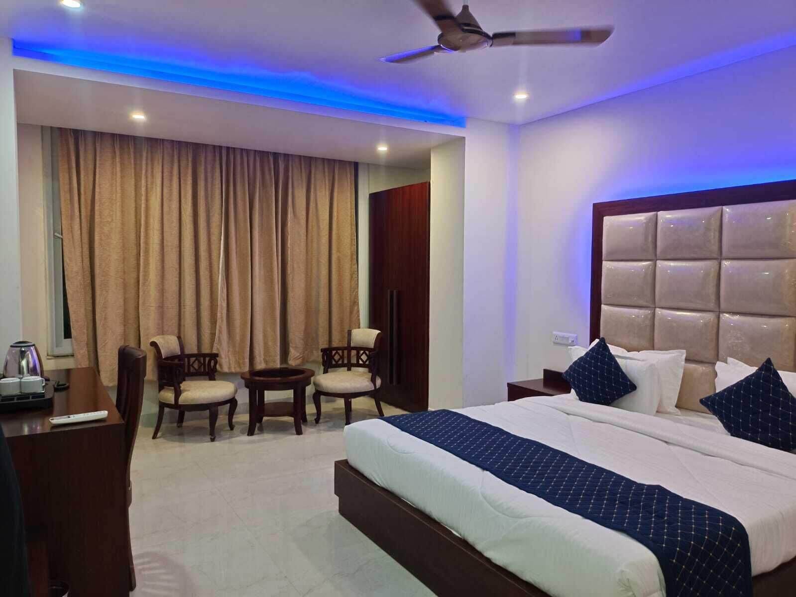 A hotel room with a bed, a desk, two chairs, a ceiling fan, and a window with curtains.