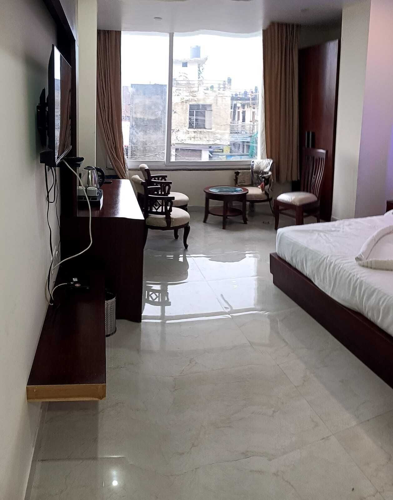 A hotel room with a bed, a desk, a chair, a small table, and a TV.
