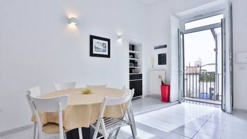 Zona pranzo con tavolo e sedie, una libreria, un termosifone e un balcone con ringhiera.