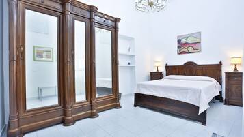 Una camera da letto con un'ampia armadio in legno, un letto con copriletto bianco, un lampadario e un quadro appeso al muro.