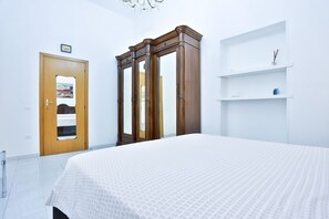 A bedroom with a bed, wooden wardrobe, white walls, and a door with a mirror.