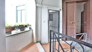 A narrow corridor with a tiled floor, a metal railing, a window with blue shutters, and a door with a metal gate. - GuestHost - B&B Lungomare Centro - Arechi Room (Salerno)
