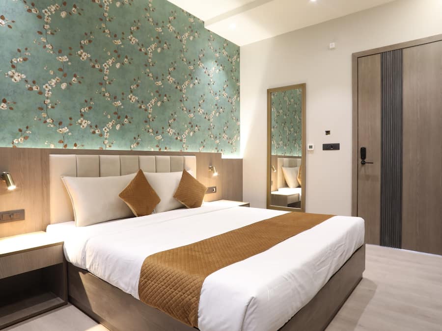 A modern hotel room with a large bed, a nightstand, a mirror, and a wardrobe.