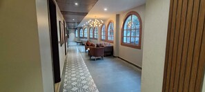 A hallway with patterned flooring, arched windows, and a seating area with sofas. - Ensober Kainchi Dham (Kosiyakutoli)