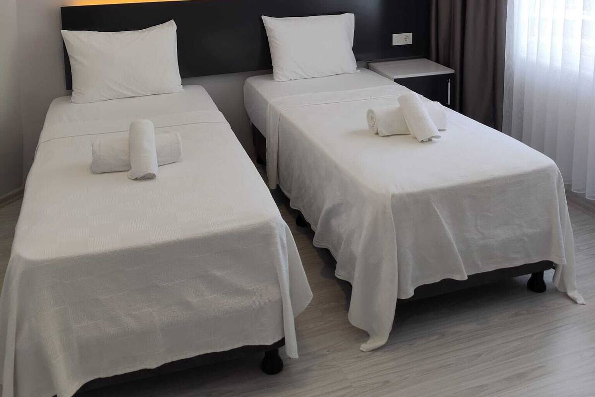 Une chambre d’hôtel avec deux lits simples, une table de chevet, une petite table et une fenêtre avec des rideaux.