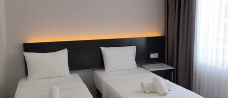 Habitación de hotel con dos camas individuales, una mesita de noche y una ventana con cortinas.
