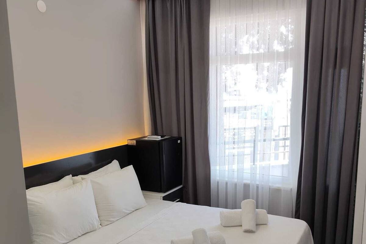 Une chambre d’hôtel avec un lit bien fait, une table de chevet avec une lampe et une fenêtre avec des rideaux.