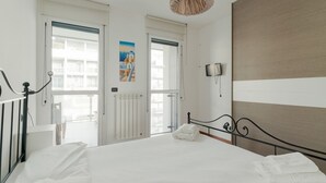 Un dormitorio con cama, puerta, televisor montado en la pared y ventana.