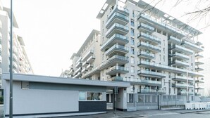 Un edificio residencial de varios pisos con balcones, una entrada con reja y una estructura pequeña adyacente.