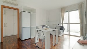 Una habitación moderna y bien iluminada con una mesa de comedor, un sofá, un refrigerador y una ventana con cortinas.