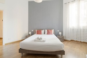 A modern bedroom with a bed, pillows, a nightstand, and a window with curtains.